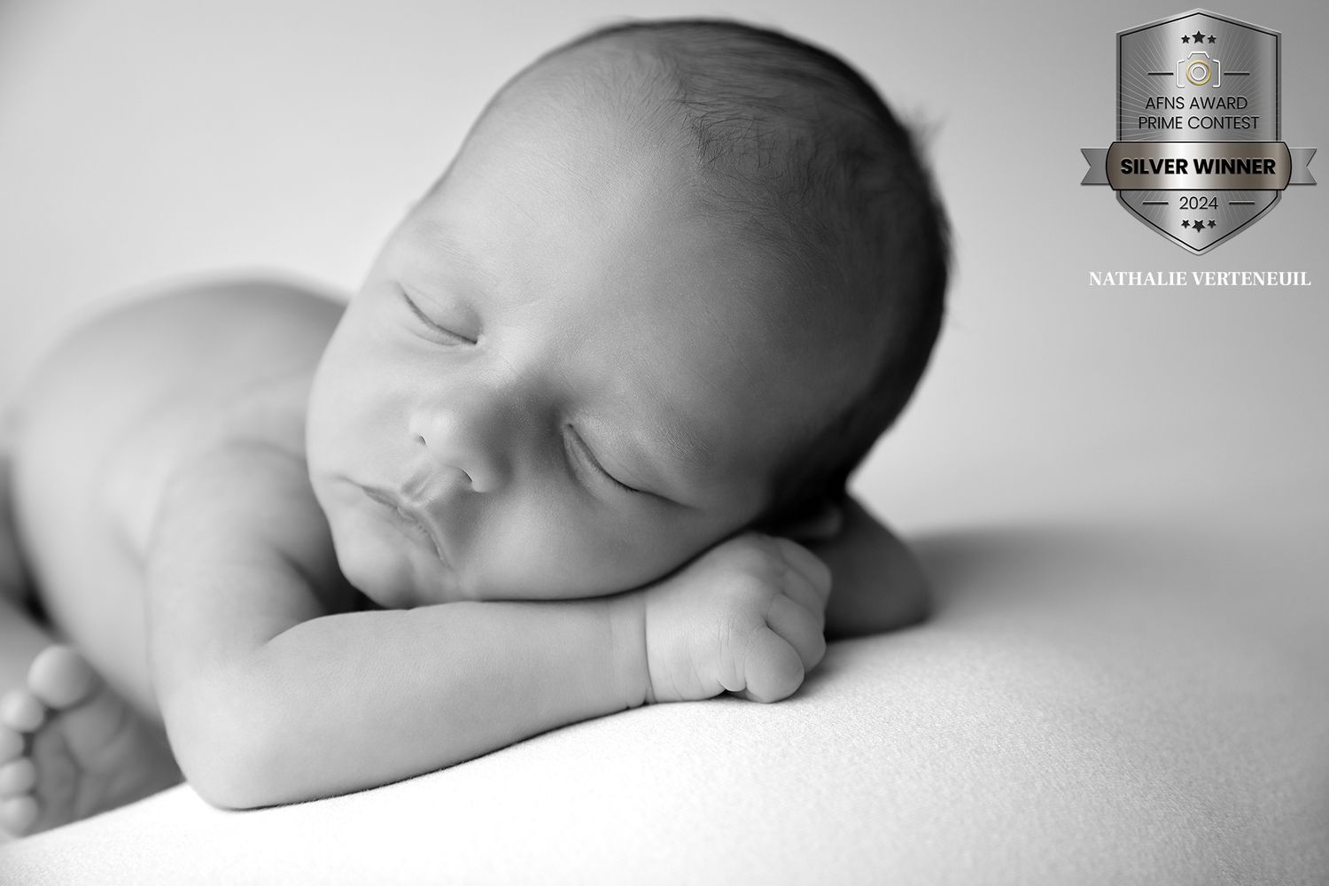 Peaceful newborn baby sleeping in black and white portrait with arms folded under head.