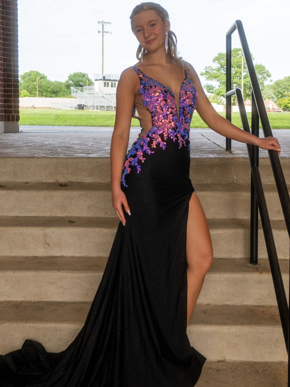 Elegant black prom dress with purple floral embellishments and thigh slit on concrete steps.