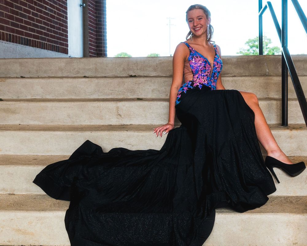 Black formal gown with purple sequined bodice and long train displayed on outdoor steps.