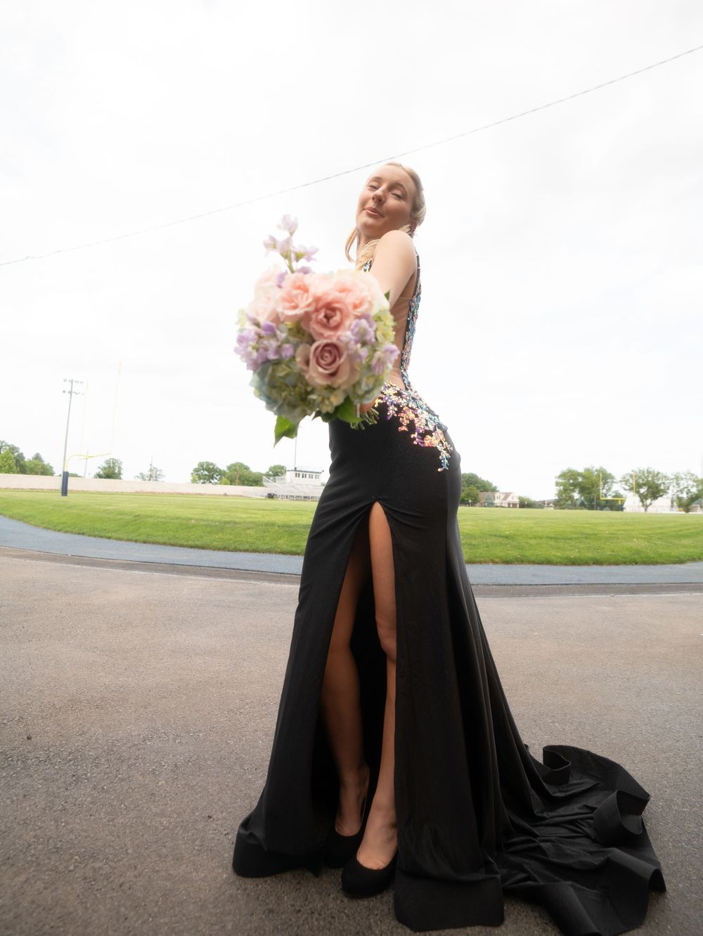 Dramatic full-length formal dress with pink roses and flowing black skirt on outdoor pathway.