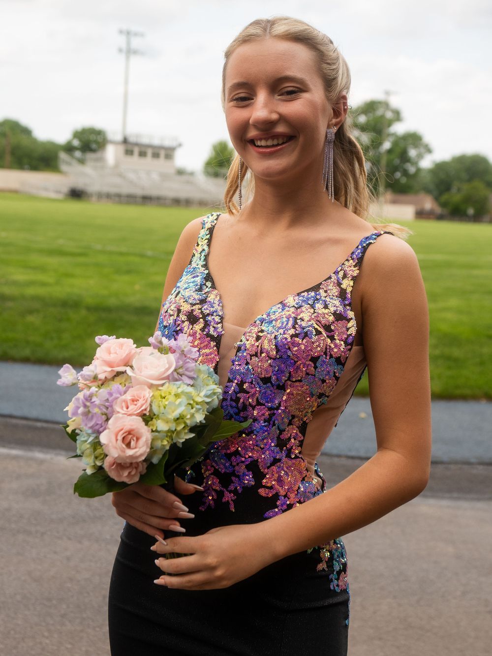 Formal gown featuring purple and pink beaded detail holding spring bouquet outdoors.