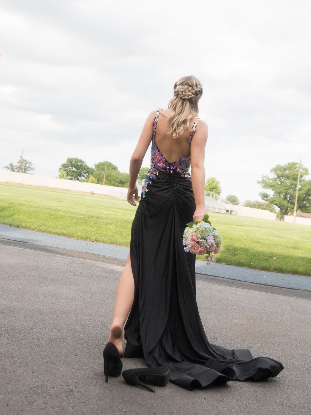 Back view of black formal gown with beaded details and trailing skirt on asphalt path.