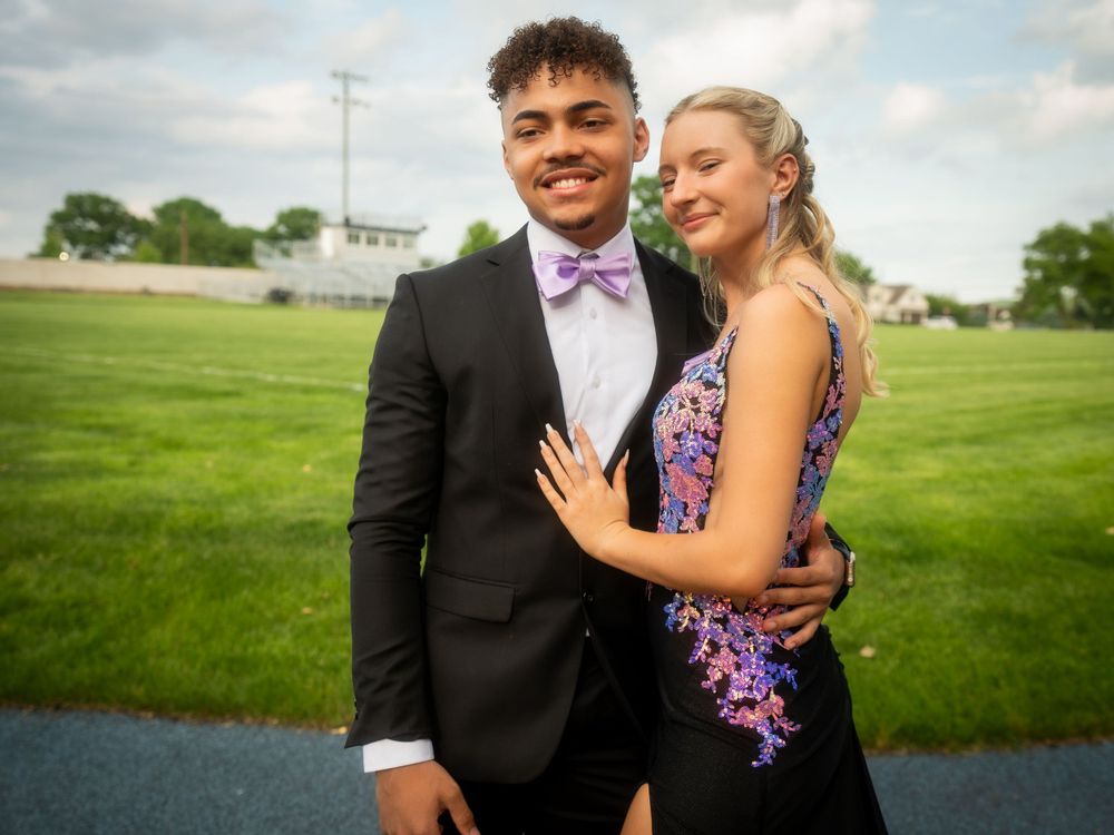 A couple poses in formal attire on a grassy field during prom photos.