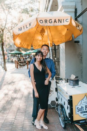 A couple stands beneath an orange organic milk umbrella next to a food cart.