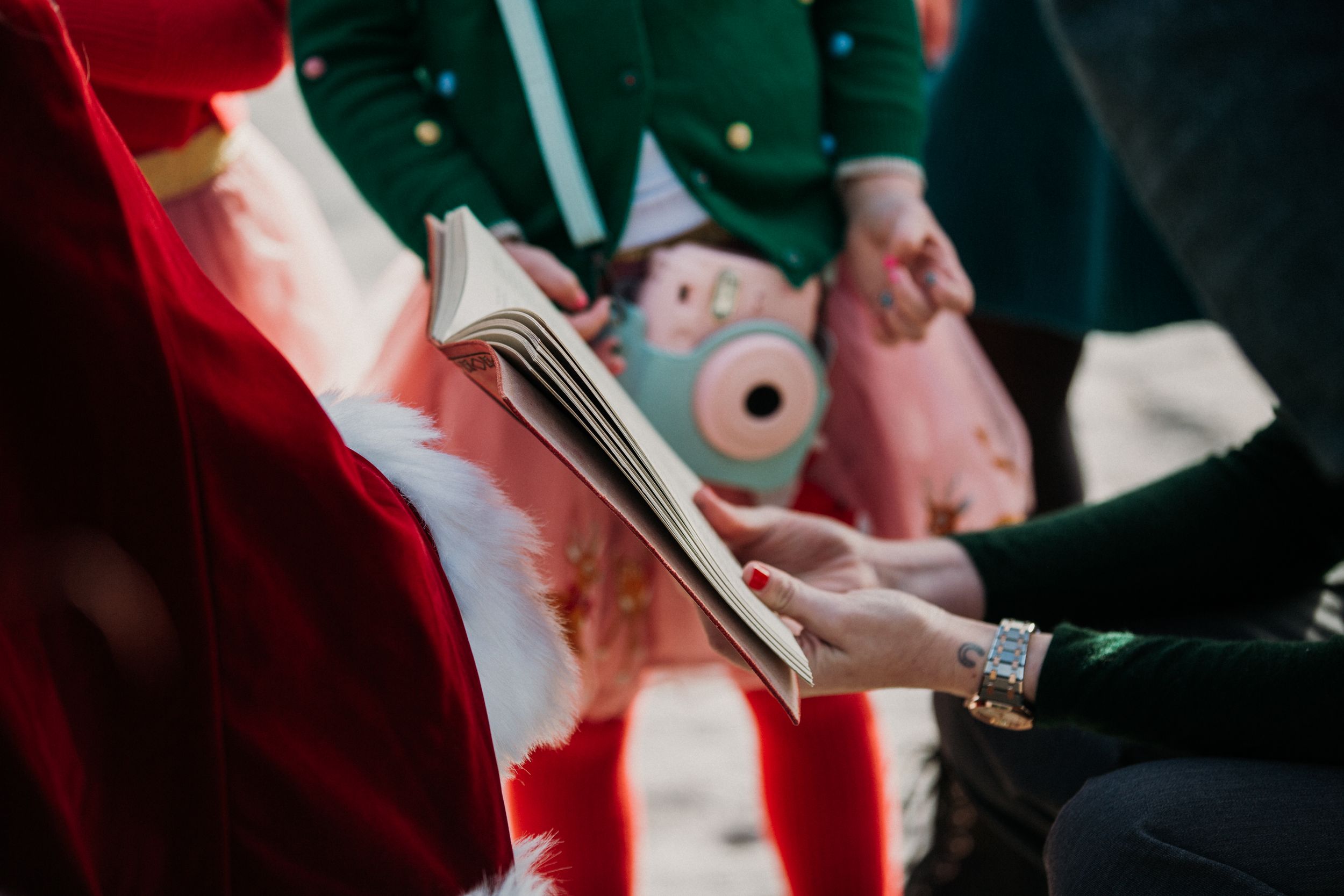 Person in red Santa suit holding a book while meeting with visitors.