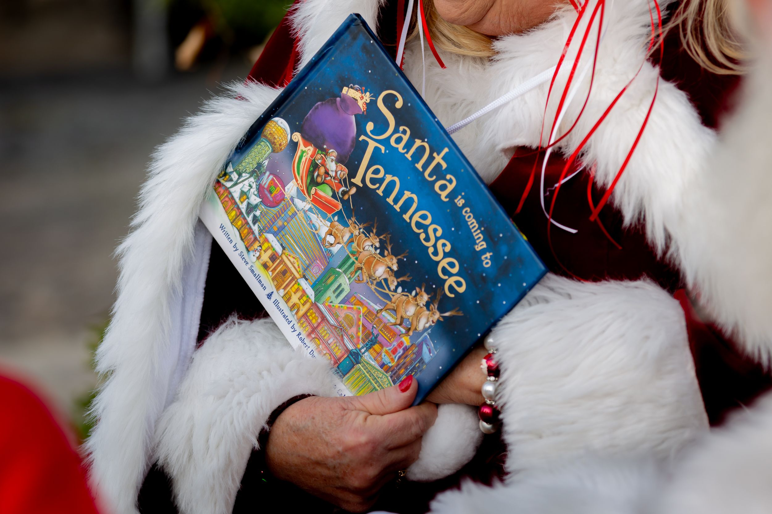 Santa costume with white fur trim holding festive storybook.