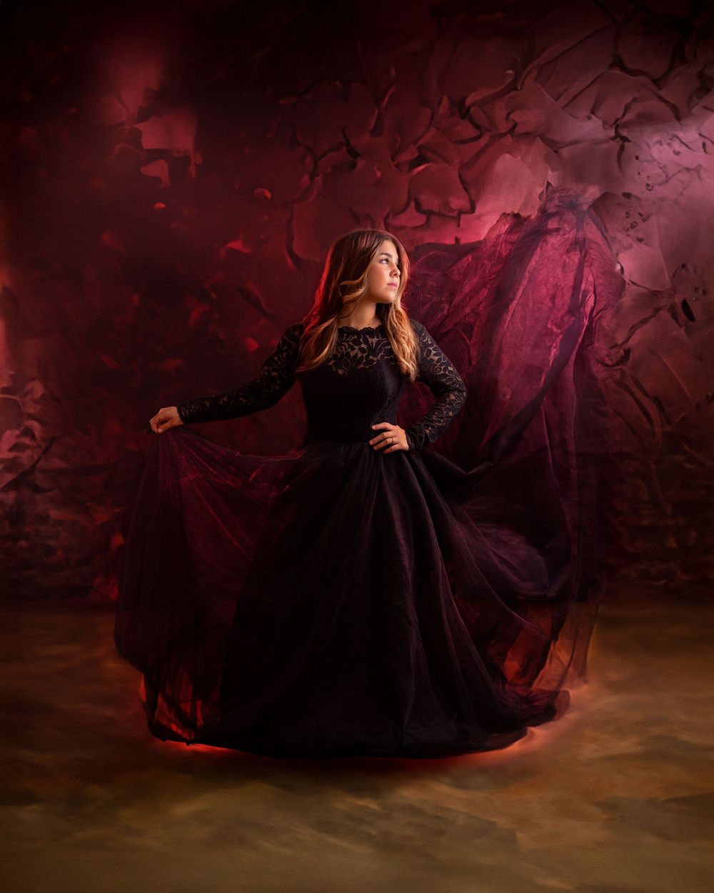 A person in a flowing black dress poses dramatically against a dark red atmospheric backdrop in a photo series.
