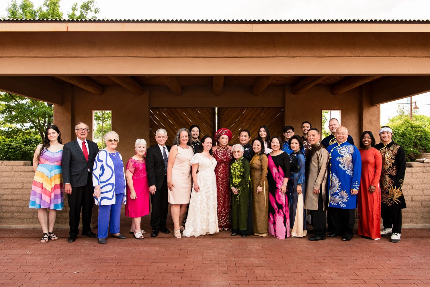Wedding party and guests gather under a covered patio wearing colorful traditional attire.