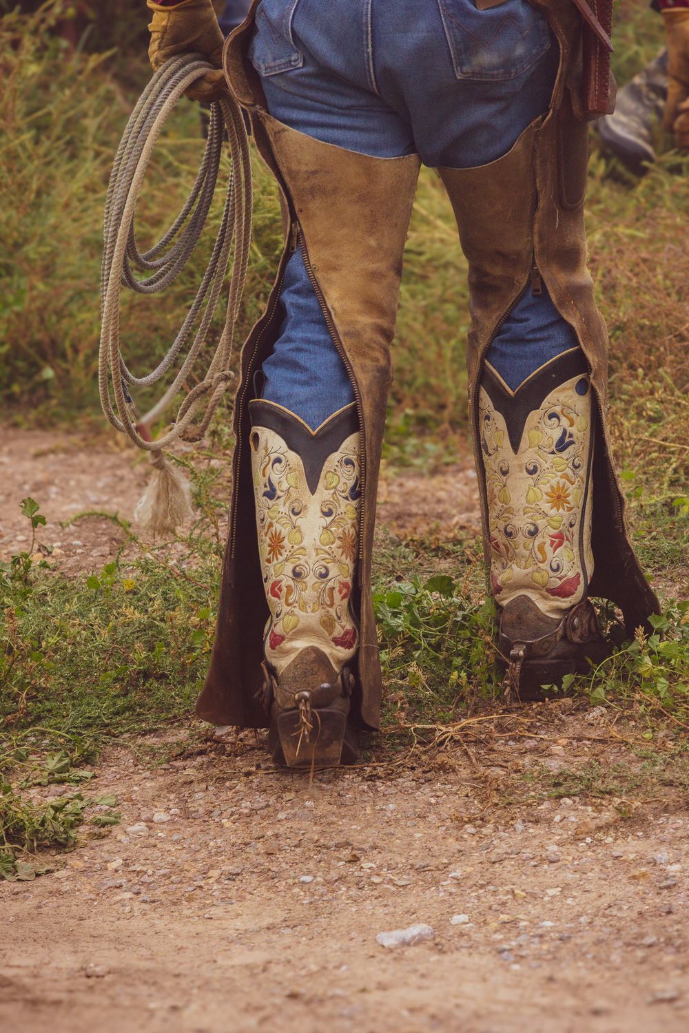 Close-up of decorative cowboy boots with embroidered designs standing on a dirt path.