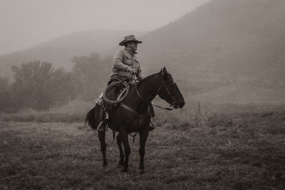 Misty landscape with riders on horseback traversing a hillside.