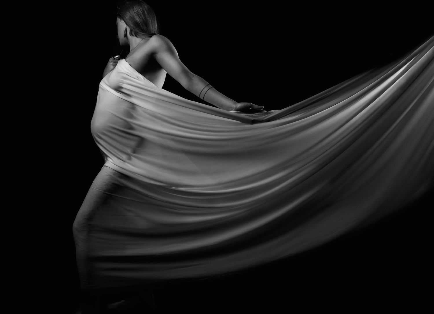 Black and white artistic dance photo featuring flowing white fabric movement against dark background.