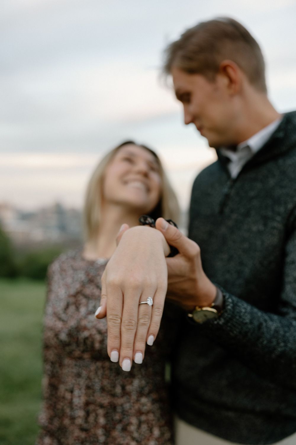 A newly engaged couple shares an intimate moment while showing off the engagement ring outdoors.