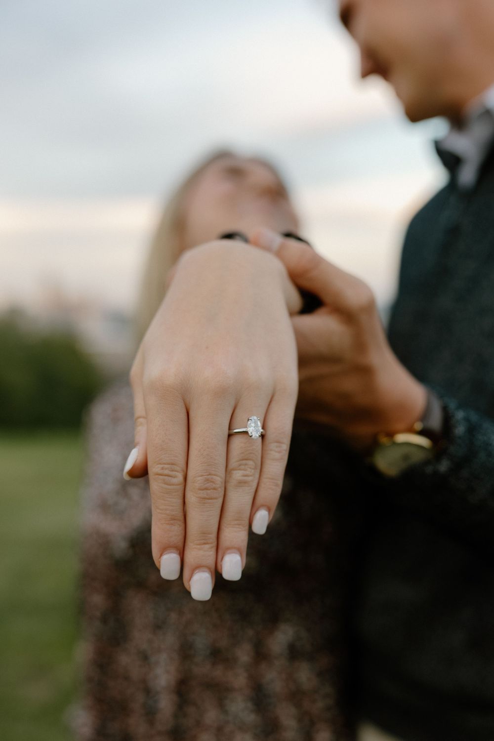 Close-up series of hands showing off a sparkling engagement ring against a blurred outdoor background.