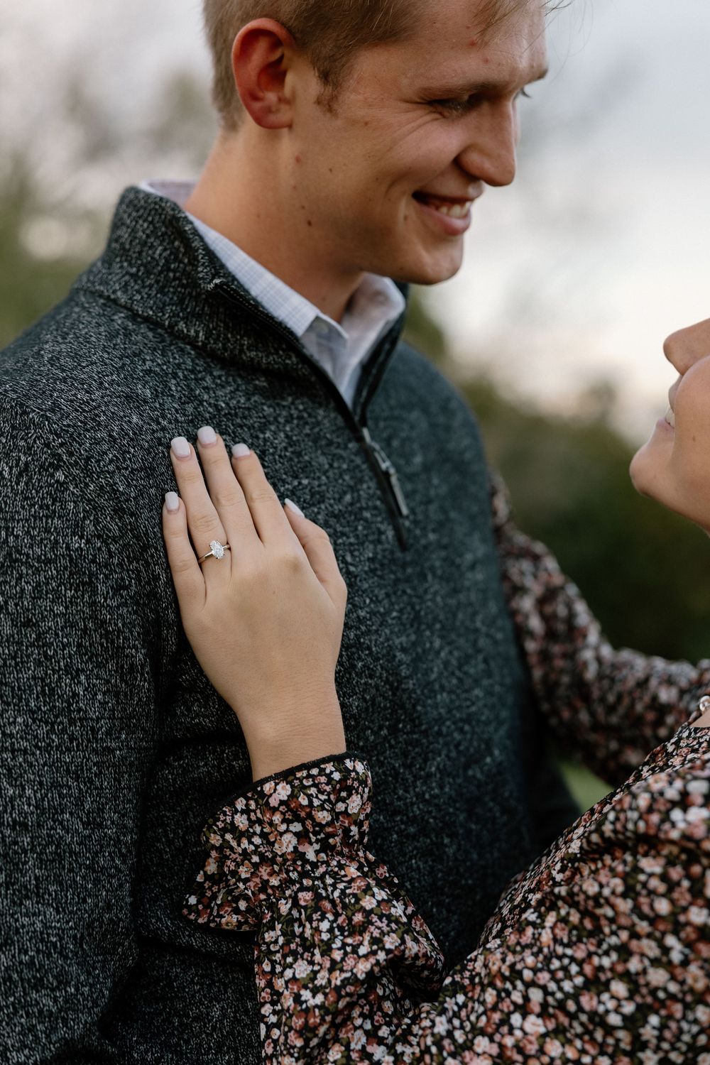 Close-up shot showing a sparkling engagement ring as a couple embraces in warm winter attire.