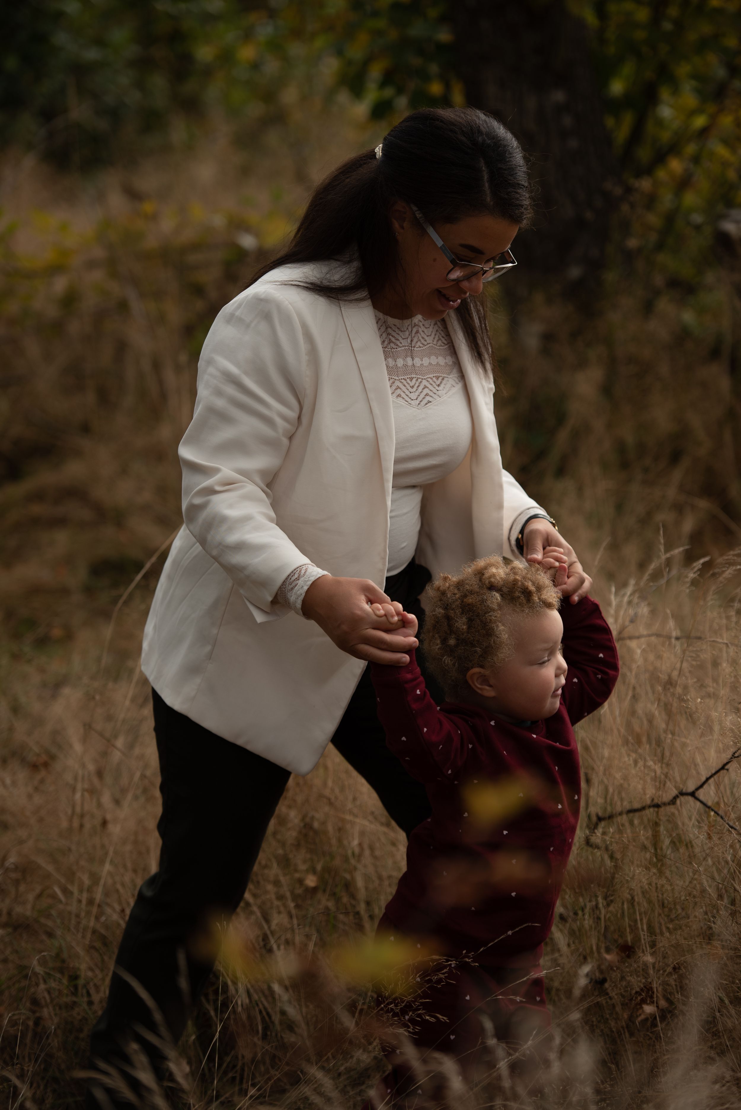 A tender moment captured in a field as a figure in a white blazer helps guide a small child in burgundy.