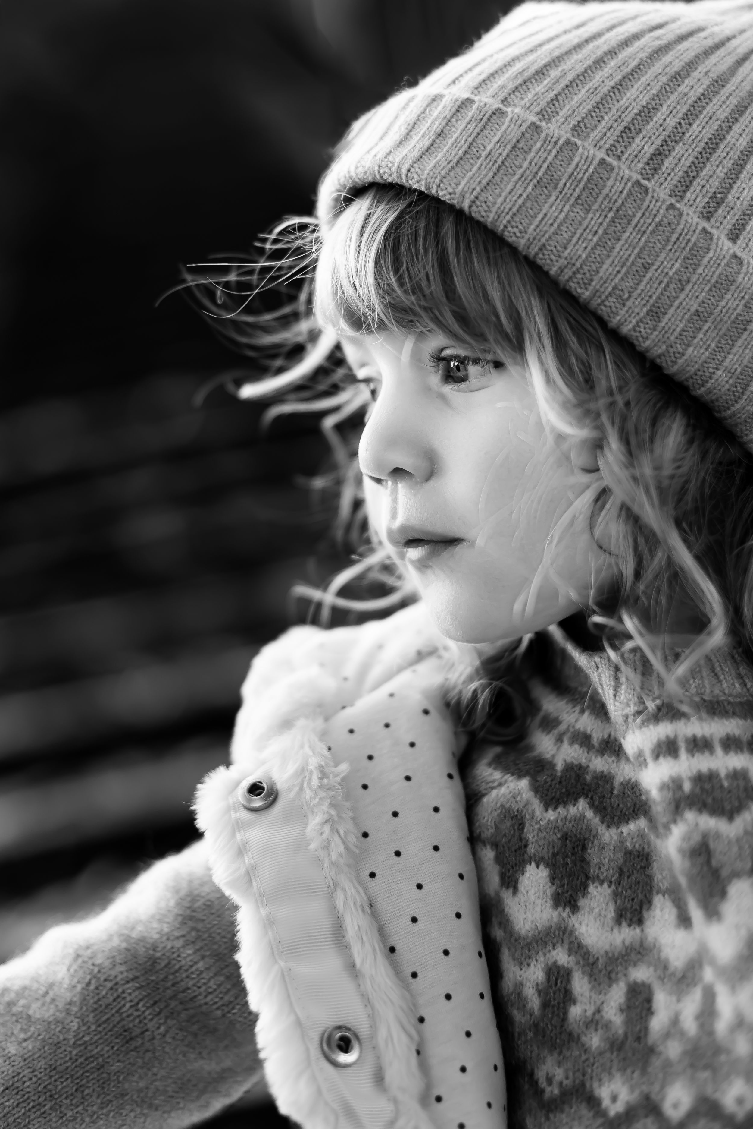 Black and white portrait of child in winter hat and patterned sweater looking to side.