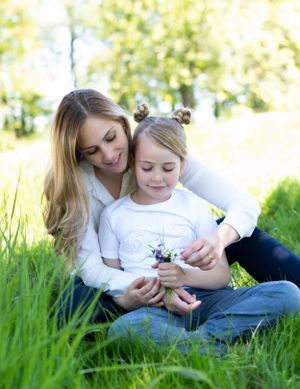 Mother and daughter sitting together in sunny grass field sharing tender moment.