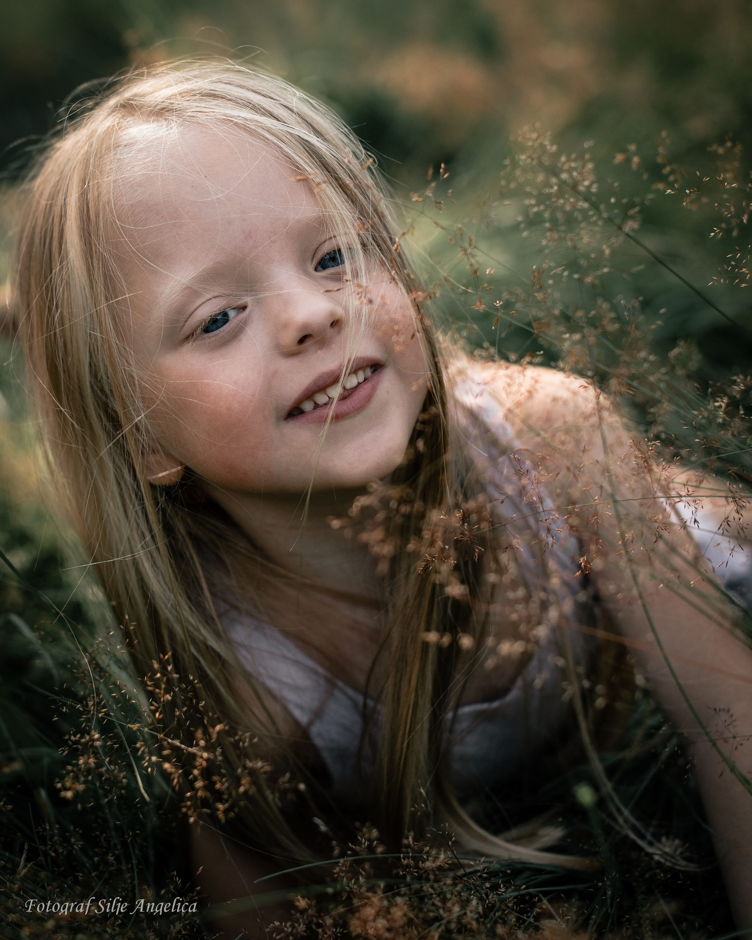 Portrait of young person in nature surrounded by delicate wildflowers and tall grass.