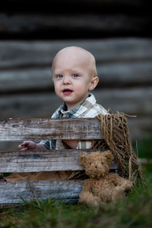 Small child peeking over rustic wooden fence outdoors.
