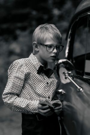 Retro style portrait of boy in polka dot shirt and glasses next to vintage car.