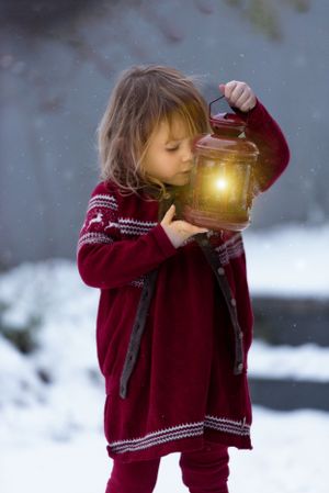 Child in red winter sweater holding glowing lantern in snowy scene.