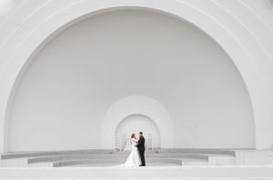Sioux City, Iowa photographer. Elegant wedding couple stands beneath grand white arched architecture in a stunning minimalist venue.