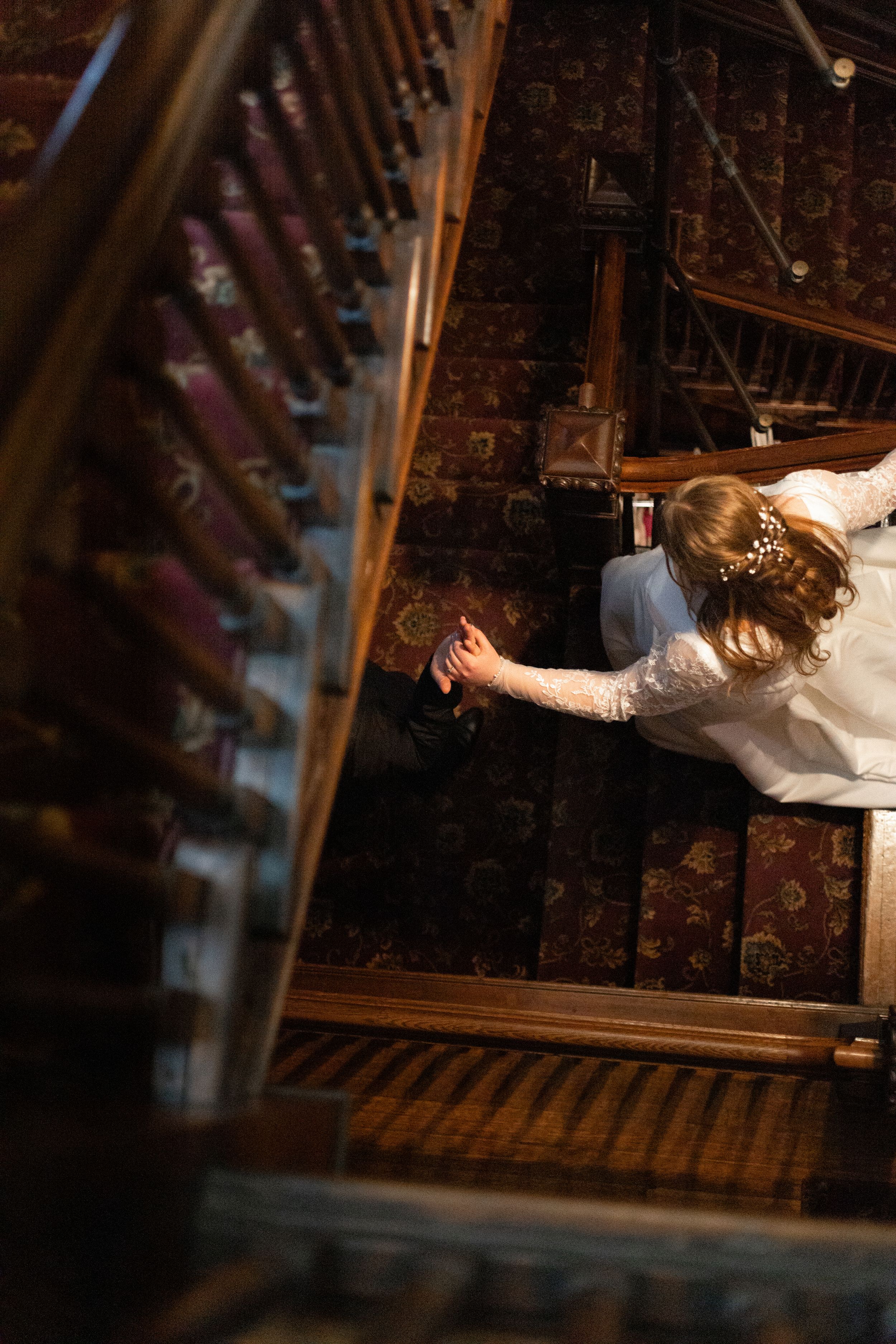 Sioux City, Iowa photographer. Aerial view of a bride in a white gown descending an ornate wooden staircase with patterned carpet.