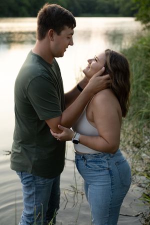 Sioux City, Iowa photographer. A couple shares a romantic moment by a tranquil lake at golden hour, the man cradling her face.