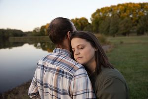 Sioux City, Iowa photographer. Woman resting her head on a man's shoulder near a peaceful lake at sunset in an intimate embrace.