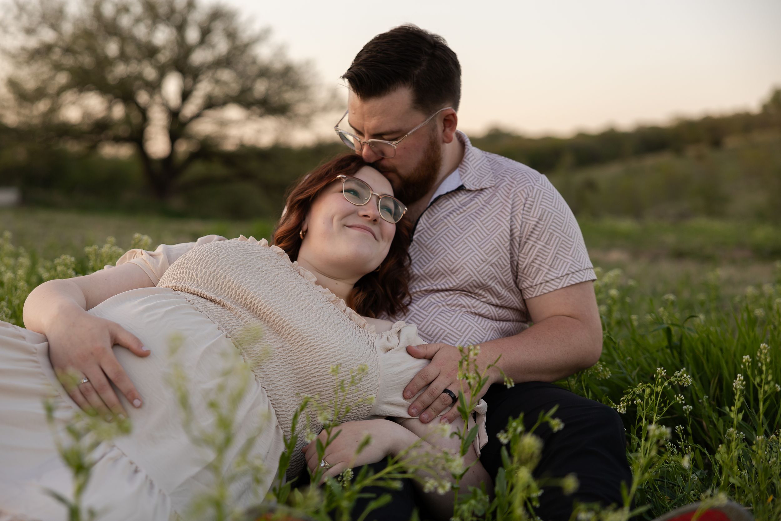 Sioux City, Iowa photographer. A couple relaxes together in a wildflower meadow at sunset, sharing a gentle kiss on the forehead.