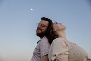 Sioux City, Iowa photographer. A couple stands back to back under a moonlit sky at dusk, the woman tilting her head back joyfully.