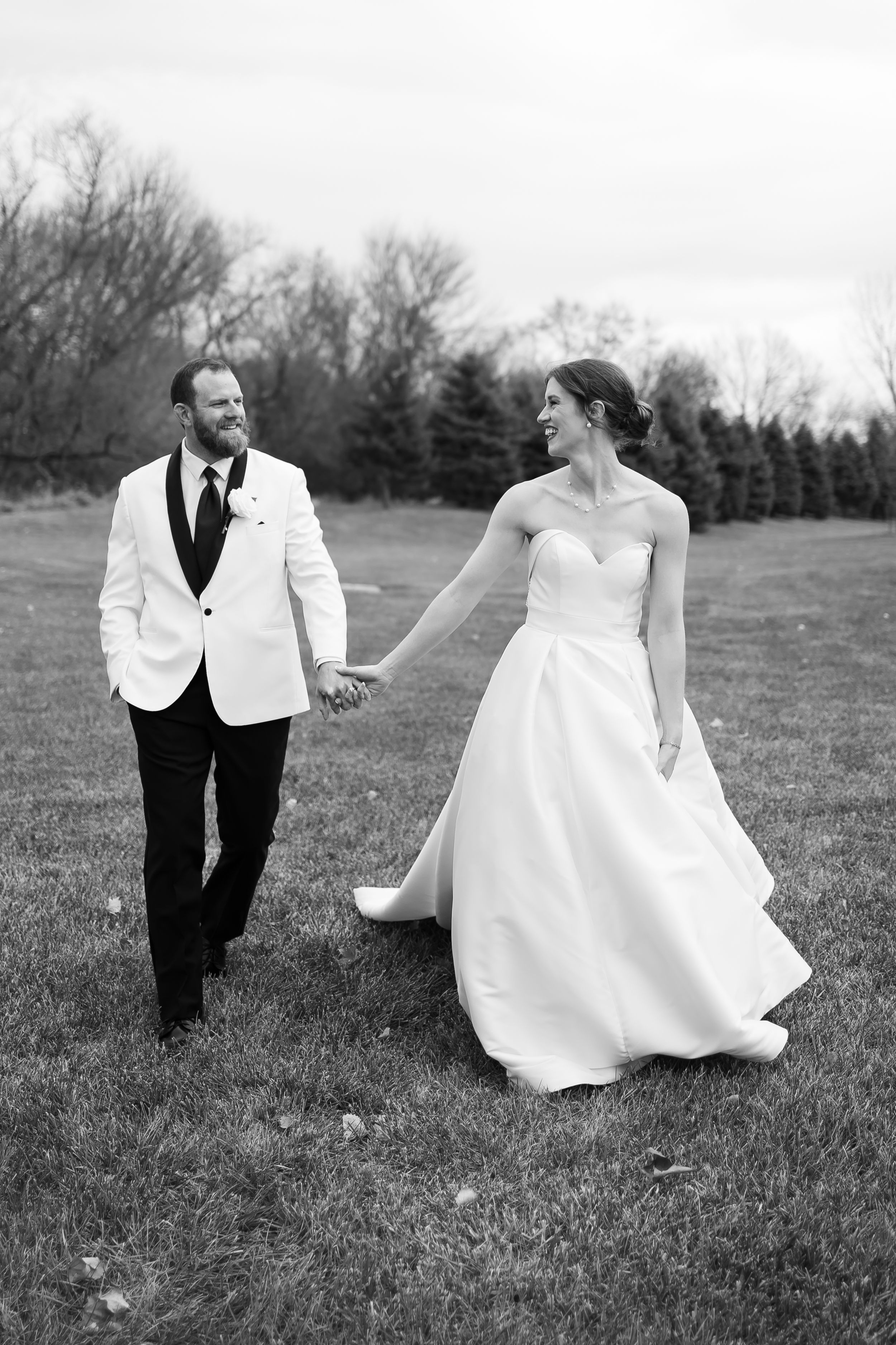 Sioux City, Iowa photographer. Black and white photo of a smiling bride and groom holding hands while walking across a grassy field.