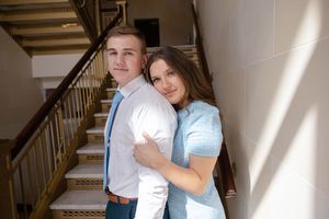 Sioux City, Iowa photographer. A young couple poses lovingly on a staircase, the woman embracing the man in a bright indoor setting.