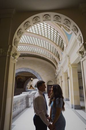 Sioux City, Iowa photographer. A romantic couple holds hands under elegant arched ceilings of a grand historic building interior.