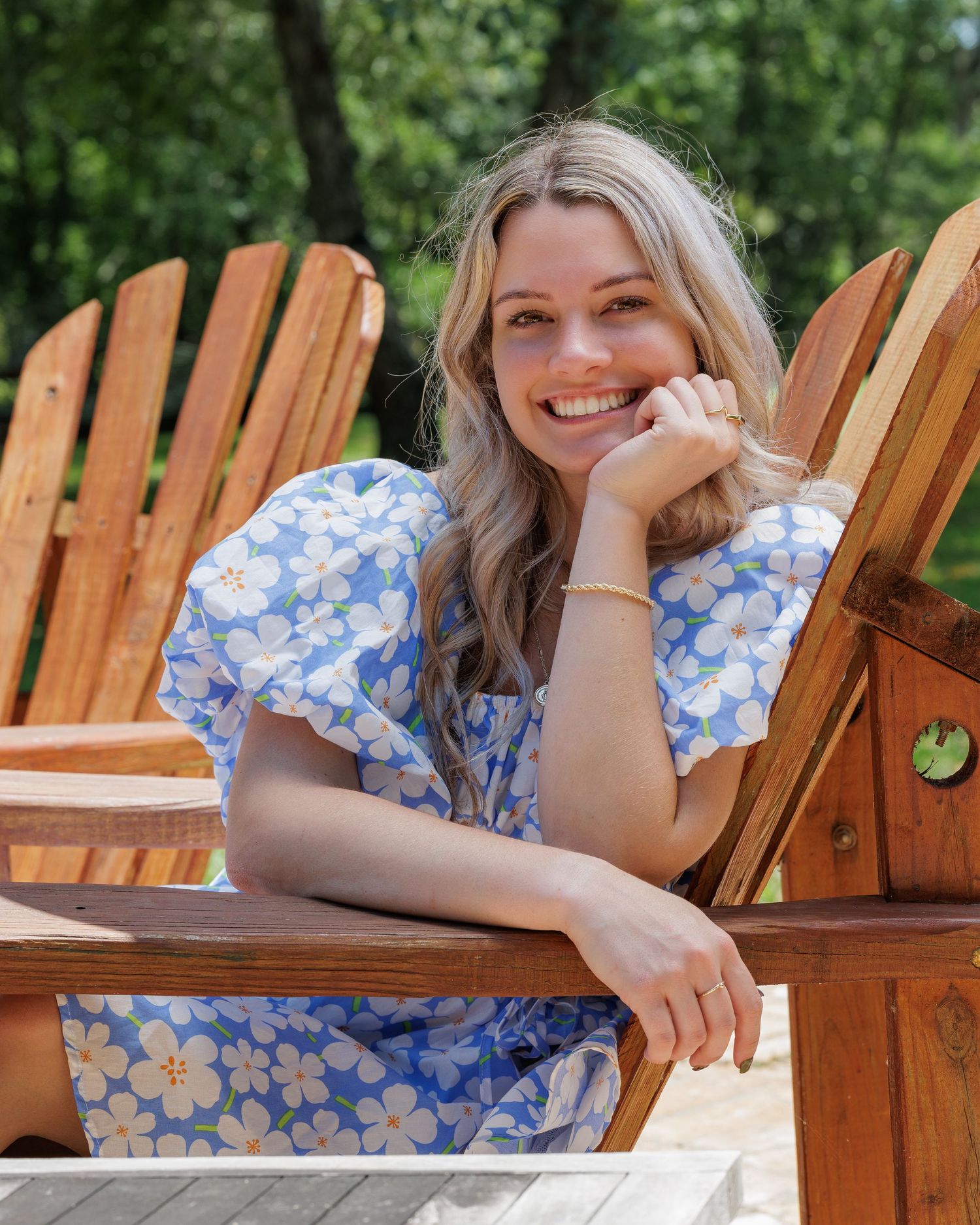Someone in blue floral dress relaxing in wooden Adirondack chair outdoors.