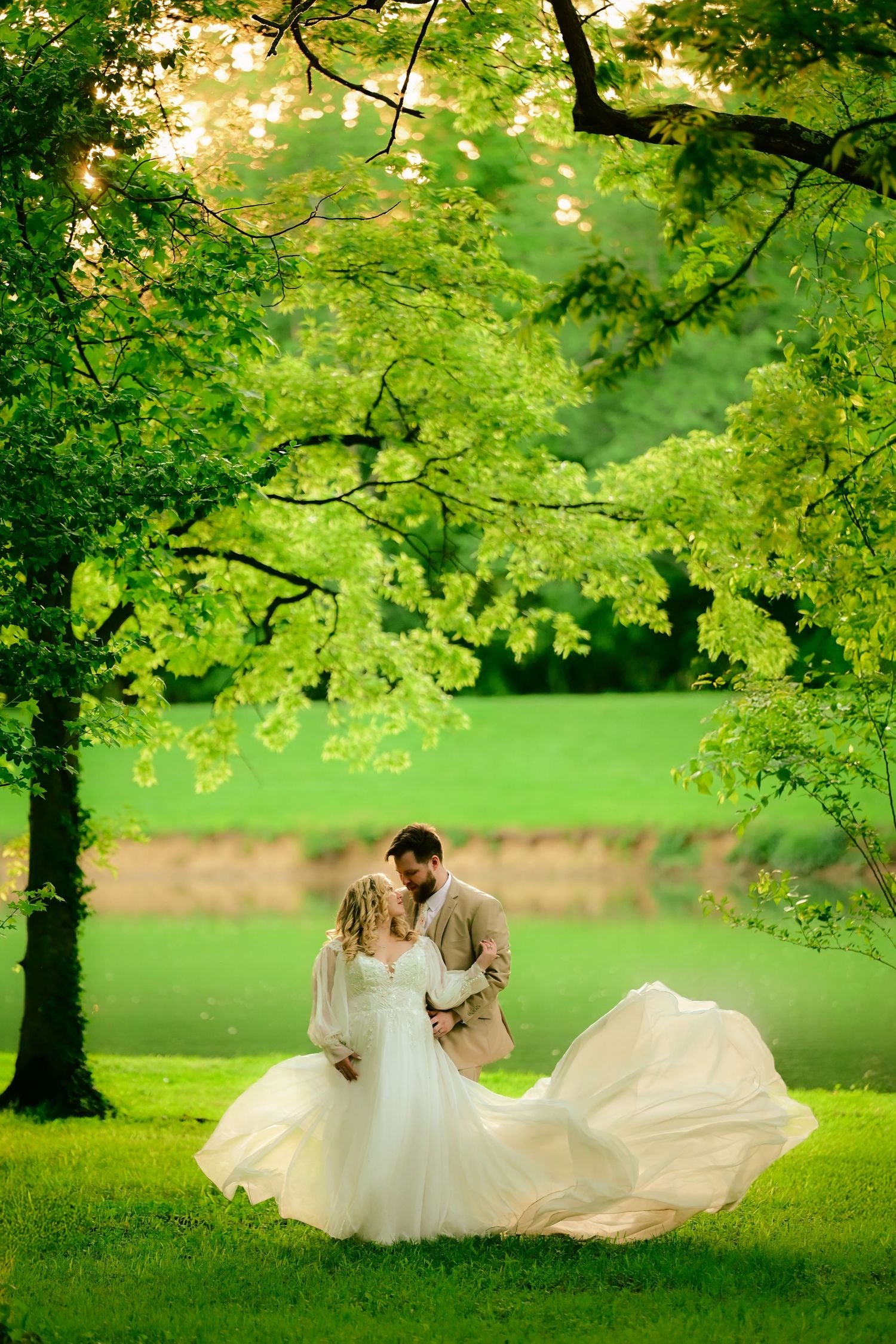 A romantic scene under vibrant green trees with flowing white gown in a lush spring garden setting.