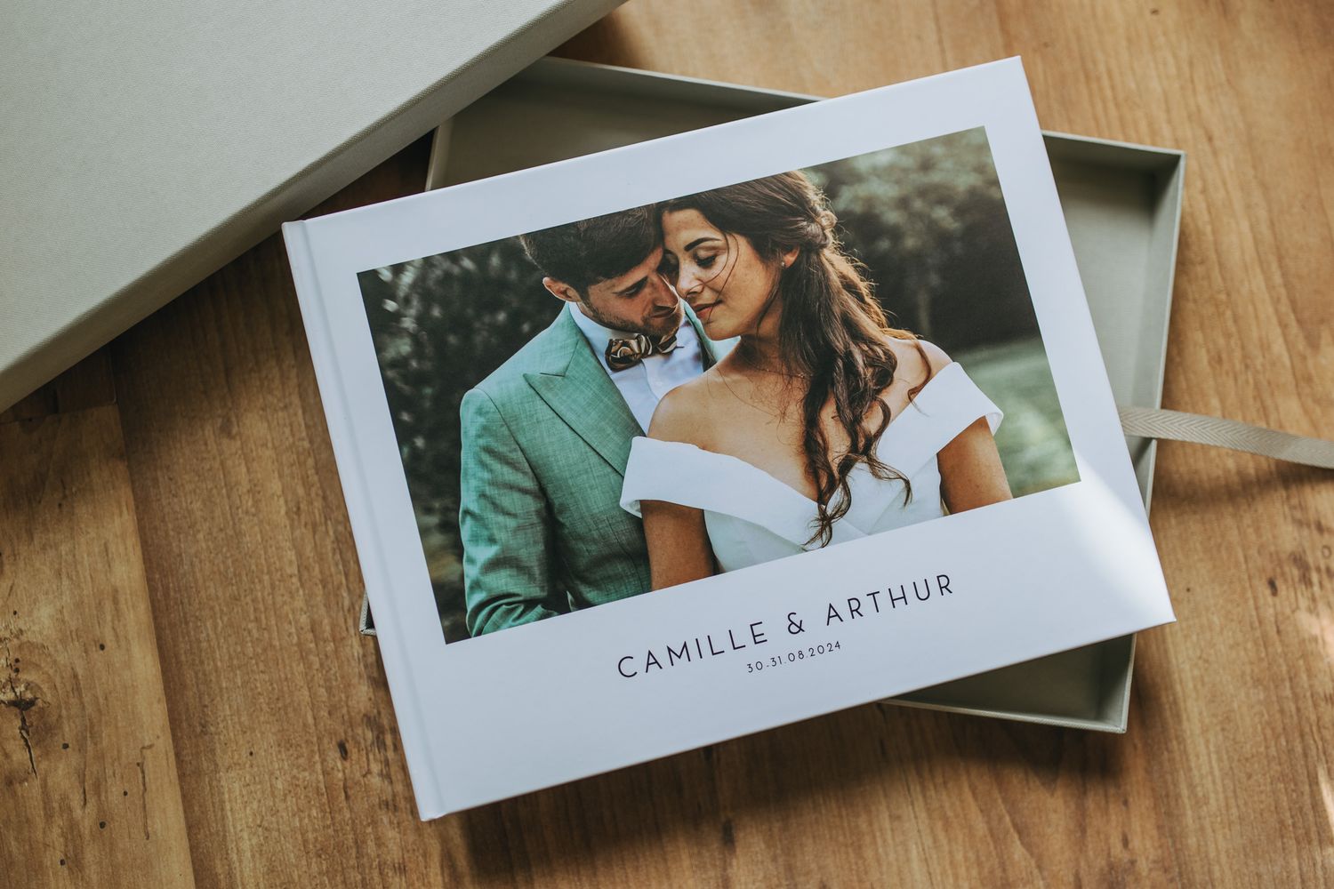 Wedding photo album pages spread across a rustic wooden table showing romantic couple moments in soft lighting.