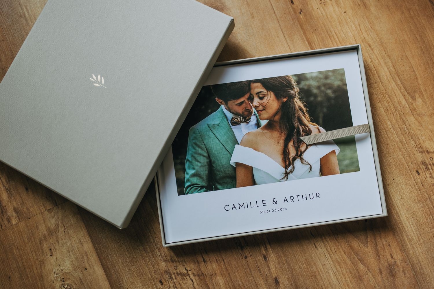 Wedding photo album with grey box and romantic couple photograph displayed on wooden floor.
