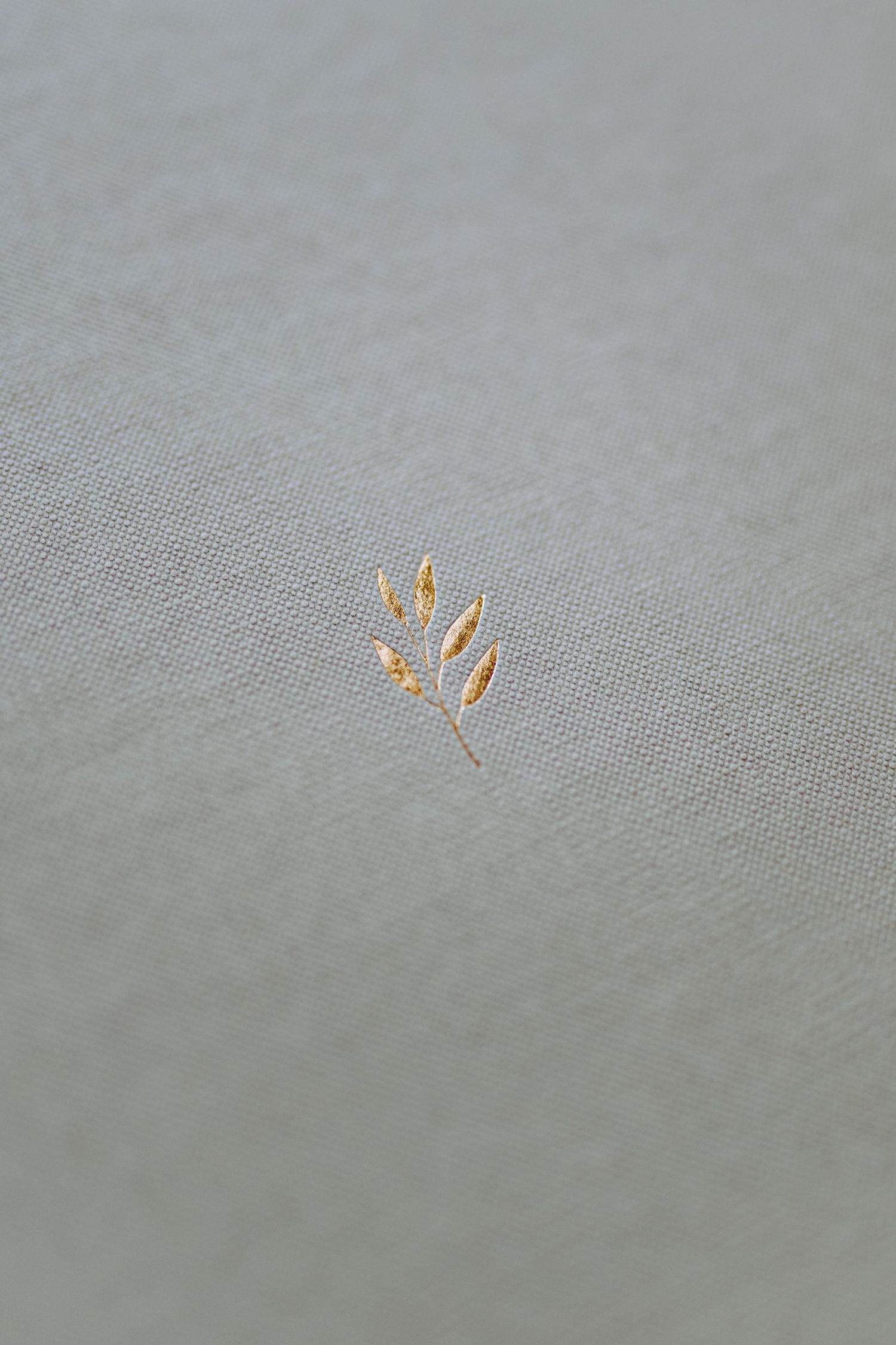 A delicate golden wheat or leaf embroidery detail on light gray fabric.