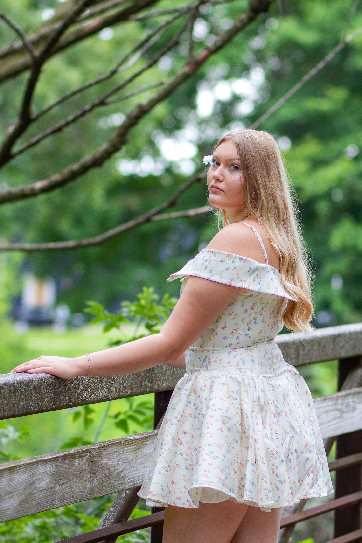 Romantic outdoor portrait series in white floral dress posed along rustic wooden fence.