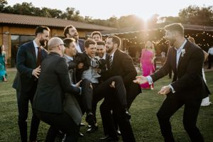 Group of formally dressed people dancing and celebrating outdoors at sunset.