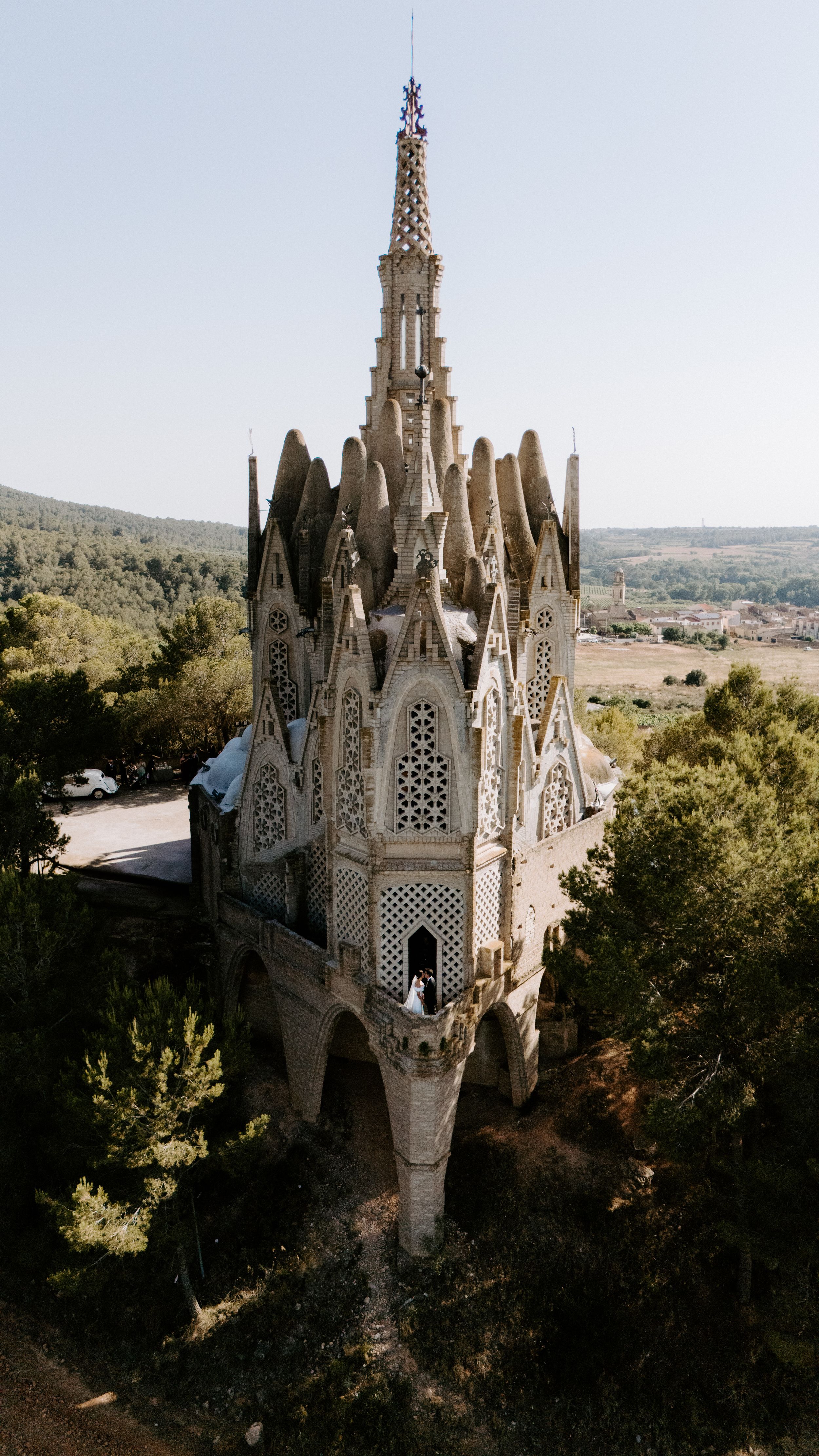 Gothic church spires rise above trees against a blue sky in Barcelona, showcasing ornate architectural details.