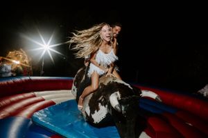 Partygoer rides mechanical bull at nighttime event with dramatic lighting and motion effects.