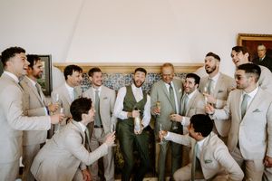 Groom and groomsmen in tan suits celebrating together, laughing and toasting with champagne glasses at a wedding.
