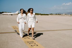 Two people in white outfits walking together on sunny beach boardwalk.