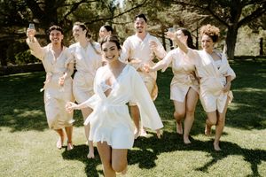 Wedding party in white outfits jumping joyfully together on a sunny lawn.