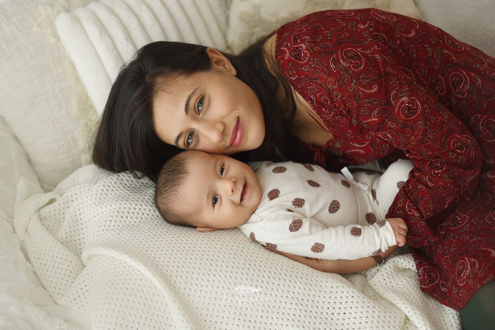A person wearing a white polka dot top lying on white bedding with a red decorative pillow in the background.