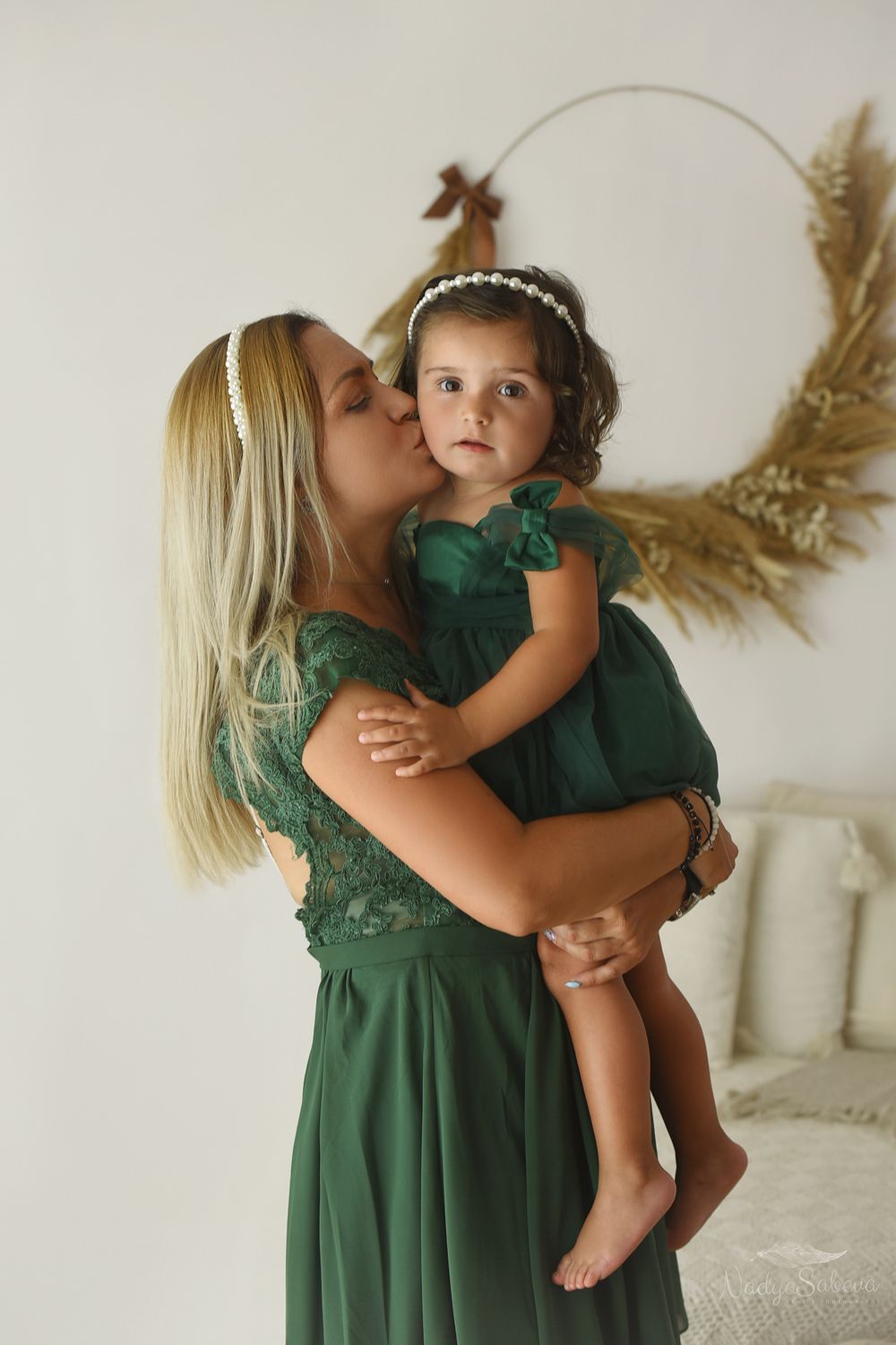 A tender moment captured in emerald green dresses against a light neutral background with dried pampas grass decor.