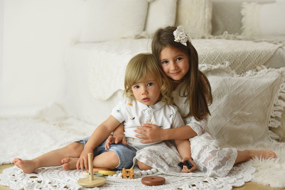 Child lying on white feathers and pillows during playful cozy photo session at home.