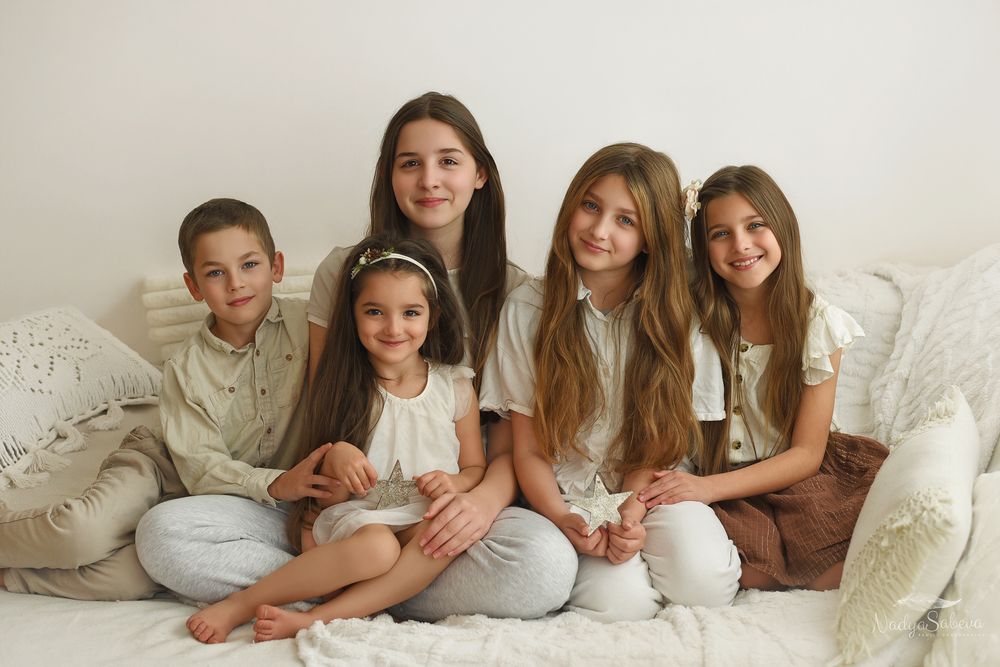 A group in coordinated white and brown outfits poses together on a light colored couch for a family portrait.